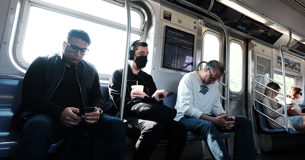 People sitting on the subway, one of them is masked