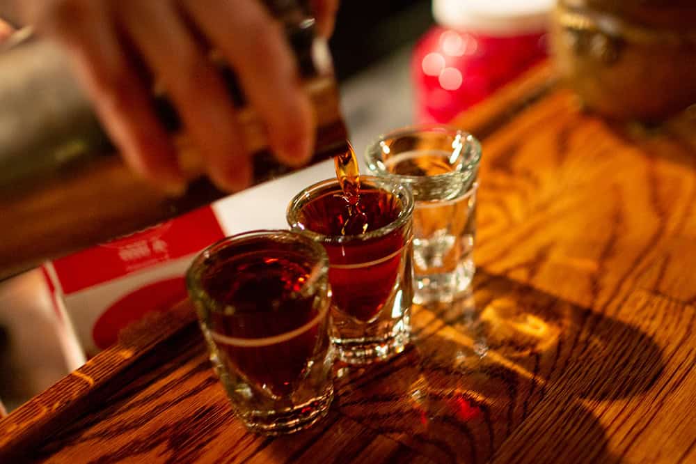 Whiskey being poured into shot glasses on bar