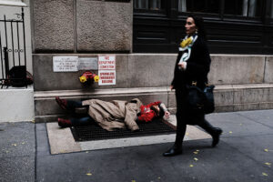 A woman walks by a homeless man along a Manhattan street