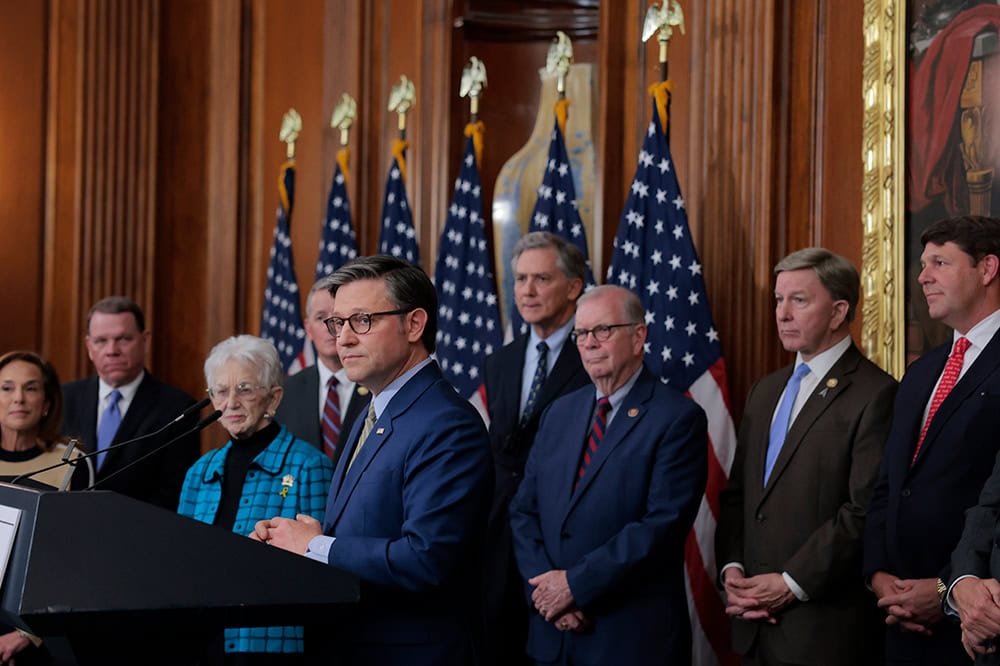 House Speaker Mike Johnson at a podium surrounded by lawmakers.