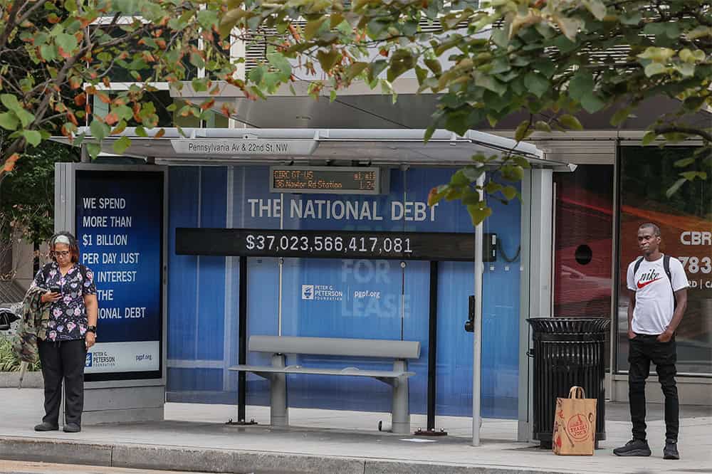 A view of a bus shelter at Pennsylvania Avenue and 22nd Street NW where an electronic billboard and a poster display the current U.S. National debt per person and as a nation in Washington, DC.