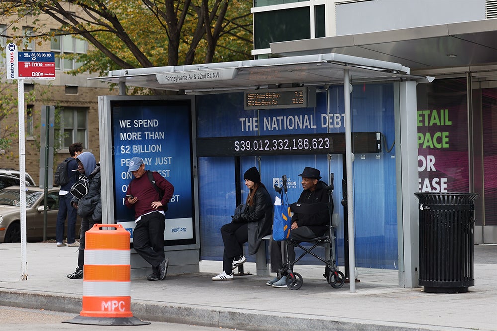A view of a bus shelter where an electronic billboard and a poster display the current U.S. National debt per person and as a nation in Washington, DC.